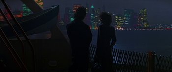 Movie still from “Joe Versus the Volcano” (1990), directed by John Patrick Shanley – Two people are standing in front of a city skyline at night; Wide shot, Over the shoulder angle