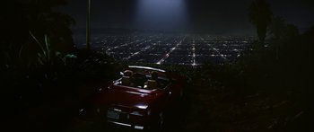 Two people in a red car at night with a city in the background