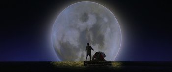 Movie still from “Joe Versus the Volcano” (1990), directed by John Patrick Shanley – A man standing in front of a tent in front of a large moon; Extreme Wide shot, Low angle