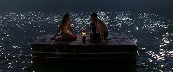 Movie still from “Joe Versus the Volcano” (1990), directed by John Patrick Shanley – A man and a woman sitting on a dock at night; Wide shot, High angle
