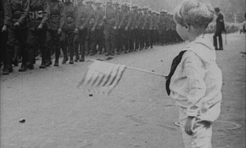 Movie still from “Johnny Got His Gun” (1971), directed by Dalton Trumbo – A young boy holding an american flag in front of a line of soldiers; Wide shot, High angle