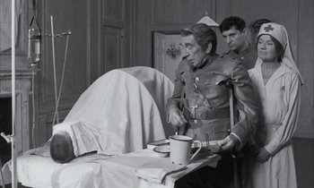 Movie still from “Johnny Got His Gun” (1971), directed by Dalton Trumbo – An old man in a uniform is standing next to a bed; Medium shot, Over the shoulder angle