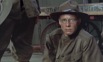 Movie still from “Johnny Got His Gun” (1971), directed by Dalton Trumbo – A man in a hat and glasses sitting in front of another man; Close Up shot, Over the shoulder angle