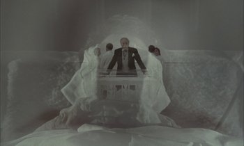 Movie still from “Johnny Got His Gun” (1971), directed by Dalton Trumbo – A man in a suit and tie standing in front of two other people; Wide shot, High angle