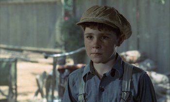 Movie still from “Johnny Got His Gun” (1971), directed by Dalton Trumbo – A young boy wearing a brown hat and suspenders looks at the camera; Close Up shot, Over the shoulder angle