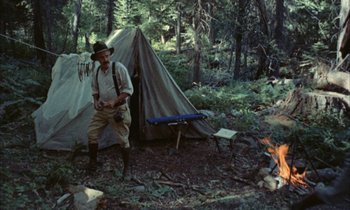Movie still from “Johnny Got His Gun” (1971), directed by Dalton Trumbo – A man standing in front of a tent in the woods; Wide shot, High angle