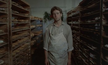Movie still from “Johnny Got His Gun” (1971), directed by Dalton Trumbo – A man standing in front of shelves of baked goods; Medium shot, Low angle