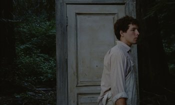 Movie still from “Johnny Got His Gun” (1971), directed by Dalton Trumbo – A young man standing in front of a wooden door; Medium shot, Low angle