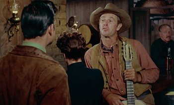 Movie still from “Johnny Guitar” (1954), directed by Nicholas Ray – A man in a cowboy hat is holding a guitar; Medium shot, Over the shoulder angle