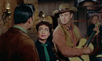 Movie still from “Johnny Guitar” (1954), directed by Nicholas Ray – Two men and a woman are sitting in front of a wall; Medium shot, Over the shoulder angle
