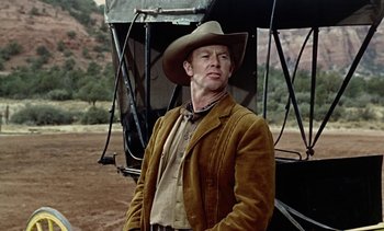 Movie still from “Johnny Guitar” (1954), directed by Nicholas Ray – A man wearing a cowboy hat standing in front of an airplane; Medium shot, Low angle