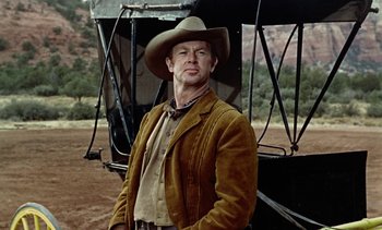 Movie still from “Johnny Guitar” (1954), directed by Nicholas Ray – A man wearing a cowboy hat standing in front of an airplane; Medium shot, Low angle