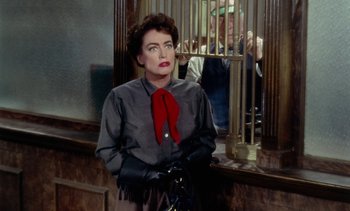 Movie still from “Johnny Guitar” (1954), directed by Nicholas Ray – A woman wearing a red neck tie standing in front of a cage; Medium shot, Over the shoulder angle