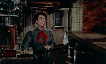 Movie still from “Johnny Guitar” (1954), directed by Nicholas Ray – A woman standing in front of a bar wearing a red neck tie; Medium shot, Over the shoulder angle