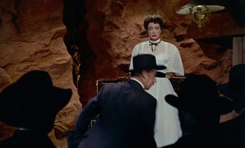 Movie still from “Johnny Guitar” (1954), directed by Nicholas Ray – A man and a woman in a white dress and black hat in front of a rock wall; Wide shot, Over the shoulder angle