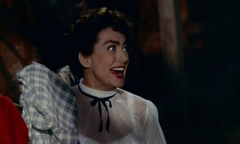 Movie still from “Johnny Guitar” (1954), directed by Nicholas Ray – A woman in a white blouse and a black bow tie smiling; Close Up shot, High angle