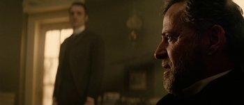 Movie still from “Jonah Hex” (2010), directed by Jimmy Hayward – A man with a goatee and a beard looking at the camera with another man in the background; Close Up shot, Over the shoulder angle