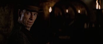 Movie still from “Jonah Hex” (2010), directed by Jimmy Hayward – A man in a hat is holding a pipe in a dark room; Close Up shot, Over the shoulder angle