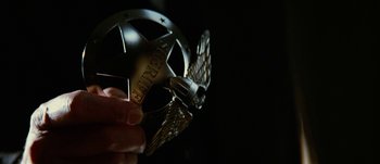 Movie still from “Jonah Hex” (2010), directed by Jimmy Hayward – A person holding a medal in front of a dark background; Extreme Close Up shot, Overhead angle