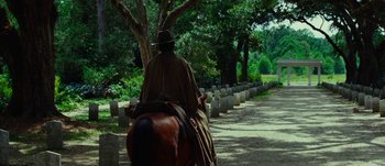 Movie still from “Jonah Hex” (2010), directed by Jimmy Hayward – A man riding a horse down a road lined with trees; Wide shot, Over the shoulder angle