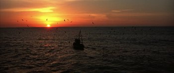 Movie still from “Jonathan Livingston Seagull” (1973), directed by Hall Bartlett – A fishing boat in the middle of the ocean at sunset; Extreme Wide shot, High angle
