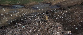 Movie still from “Jonathan Livingston Seagull” (1973), directed by Hall Bartlett – A pile of trash on the ground near a body of water; Extreme Wide shot, High angle