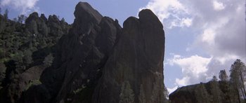 Movie still from “Jonathan Livingston Seagull” (1973), directed by Hall Bartlett – A large rock formation in front of a blue sky with some clouds; Extreme Wide shot, Low angle