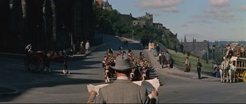 Movie still from “Journey to the Center of the Earth” (1959), directed by Henry Levin – A man in a suit and hat is looking at a marching band; Extreme Wide shot, High angle