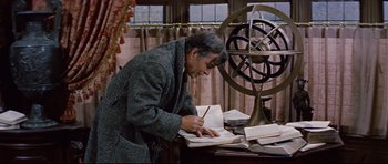 Movie still from “Journey to the Center of the Earth” (1959), directed by Henry Levin – A man writing on a book in front of an armillary sphere; Medium shot, High angle