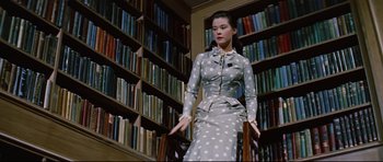 Movie still from “Journey to the Center of the Earth” (1959), directed by Henry Levin – A young woman in a polka dot dress in front of bookshelves; Medium shot, Low angle