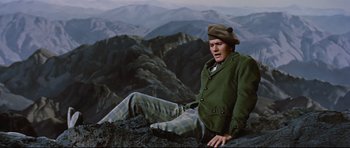 Movie still from “Journey to the Center of the Earth” (1959), directed by Henry Levin – A man sitting on top of a mountain with mountains in the background; Medium shot, High angle