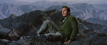 Movie still from “Journey to the Center of the Earth” (1959), directed by Henry Levin – A man sitting on top of a rock on top of a mountain; Medium shot, High angle