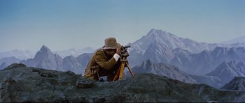 Movie still from “Journey to the Center of the Earth” (1959), directed by Henry Levin – A man in brown jacket and brown hat using a camera on top of a mountain; Wide shot, High angle