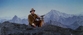 Movie still from “Journey to the Center of the Earth” (1959), directed by Henry Levin – A man sitting on top of a rock with a telescope; Wide shot, Overhead angle