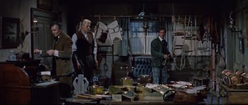 Movie still from “Journey to the Center of the Earth” (1959), directed by Henry Levin – Two men standing next to each other in front of a cluttered table; Medium shot, High angle