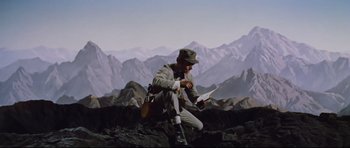 Movie still from “Journey to the Center of the Earth” (1959), directed by Henry Levin – A man sitting on top of a mountain reading a book; Wide shot, High angle