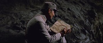 Movie still from “Journey to the Center of the Earth” (1959), directed by Henry Levin – A man sitting in front of a rock wall looking at a map; Medium shot, High angle