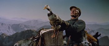 Movie still from “Journey to the Center of the Earth” (1959), directed by Henry Levin – A man holding a duck in a basket on top of a bike; Medium shot, Low angle