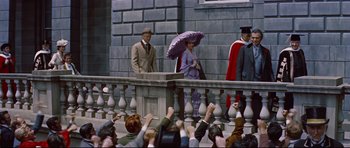 Movie still from “Journey to the Center of the Earth” (1959), directed by Henry Levin – A man holding an open umbrella next to a woman in front of a crowd of onlookers; Wide shot, High angle