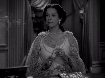 Movie still from “Juarez” (1939), directed by William Dieterle – A black - and - white photo of a woman sitting at a table; Medium shot, Over the shoulder angle