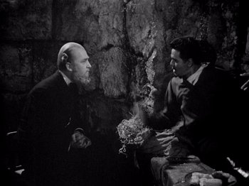 Movie still from “Juarez” (1939), directed by William Dieterle – Two men sitting on a bench in front of a stone wall; Medium shot, High angle