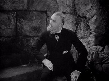 Movie still from “Juarez” (1939), directed by William Dieterle – A man in a suit sitting in front of a stone wall; Medium shot, High angle