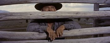 Movie still from “Jubal” (1956), directed by Delmer Daves – A man in a cowboy hat peering over a wooden fence; Medium shot, Low angle