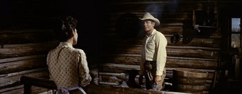 Movie still from “Jubal” (1956), directed by Delmer Daves – A man in a cowboy hat standing next to a woman; Medium shot, Over the shoulder angle
