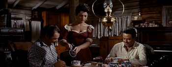 Movie still from “Jubal” (1956), directed by Delmer Daves – A woman pouring a drink into a cup at a table; Medium shot, Low angle