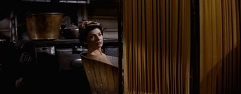 Movie still from “Jubal” (1956), directed by Delmer Daves – A woman is standing behind a curtain in a room; Medium shot, High angle