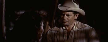 Movie still from “Jubal” (1956), directed by Delmer Daves – A man wearing a cowboy hat while standing next to a pole; Close Up shot, Over the shoulder angle