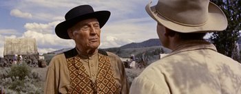 Movie still from “Jubal” (1956), directed by Delmer Daves – A man wearing a cowboy hat talking to another man in a field; Medium shot, Over the shoulder angle