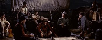 Movie still from “Jubal” (1956), directed by Delmer Daves – A group of men sitting next to each other on the ground; Wide shot, High angle