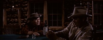 Movie still from “Jubal” (1956), directed by Delmer Daves – Two men sitting at a table with a bottle of whiskey; Medium shot, Over the shoulder angle
